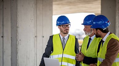 Three FM professionals in hard hats reviewing blueprints on a large construction site